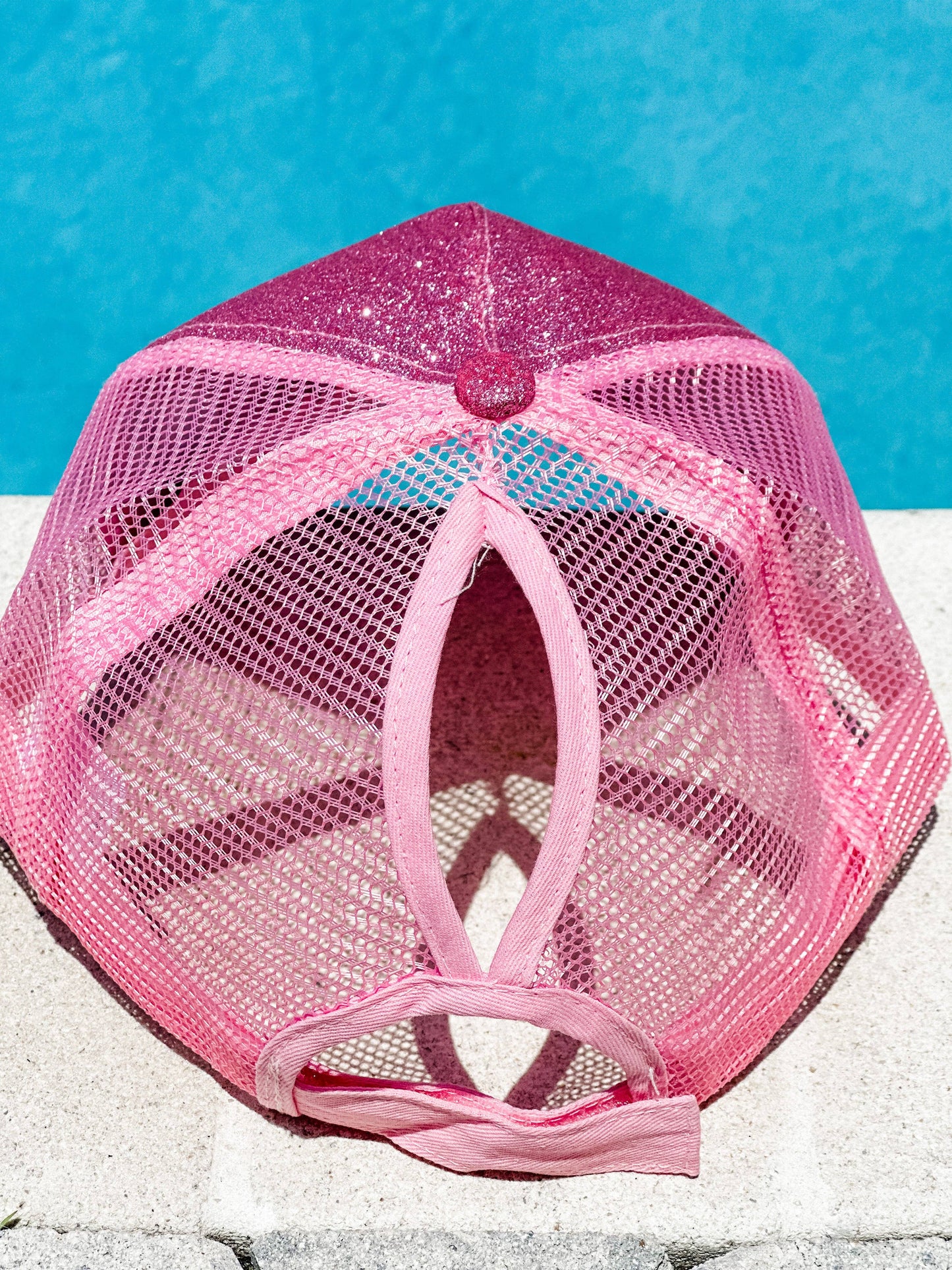 "Pink glitter trucker hat with a mesh back, displayed in front of a bright blue pool background, shown from both the front and back views."