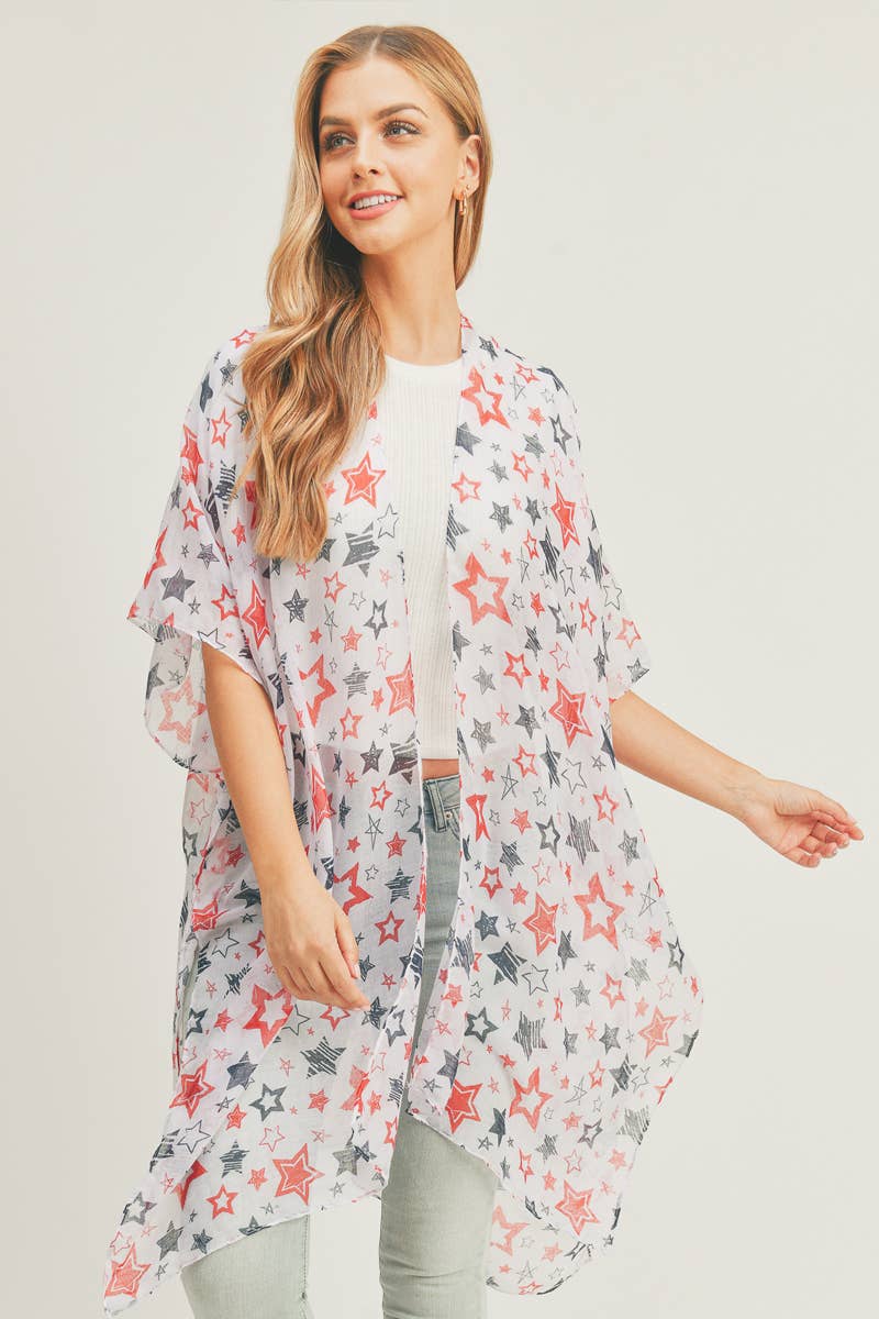 A woman modeling a lightweight, sheer kimono with a patriotic star pattern in red, navy blue, and white. The open-front kimono features a flowing, loose-fit design that drapes effortlessly over a white ribbed top and light-wash jeans. Perfect for layering during casual outings or holiday events, offering a stylish yet breezy look.