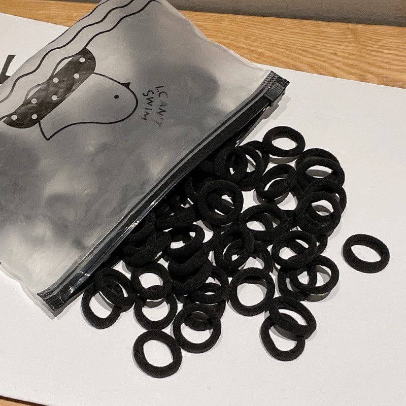 A small plastic zippered bag labeled "I Can Swim" is open, spilling out a colorful assortment of hair ties onto a white surface. The hair ties come in all black creating a vibrant and playful display.