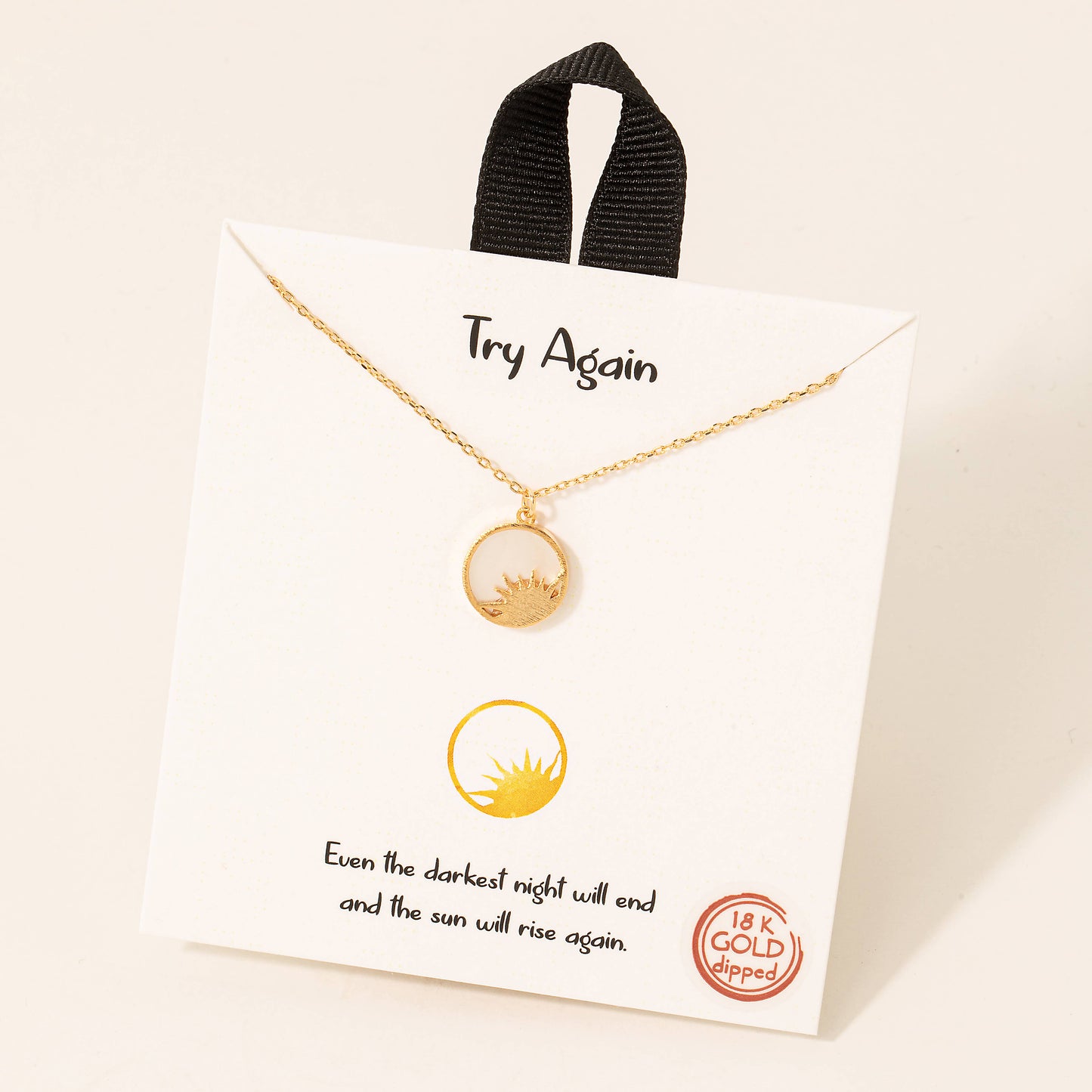 A delicate 18K gold-dipped necklace featuring a minimalist sun design enclosed within a circular pendant, symbolizing hope and resilience. Displayed on a white card with the motivational phrase "Try Again" and the quote, "Even the darkest night will end and the sun will rise again," this piece is an elegant and inspirational accessory.