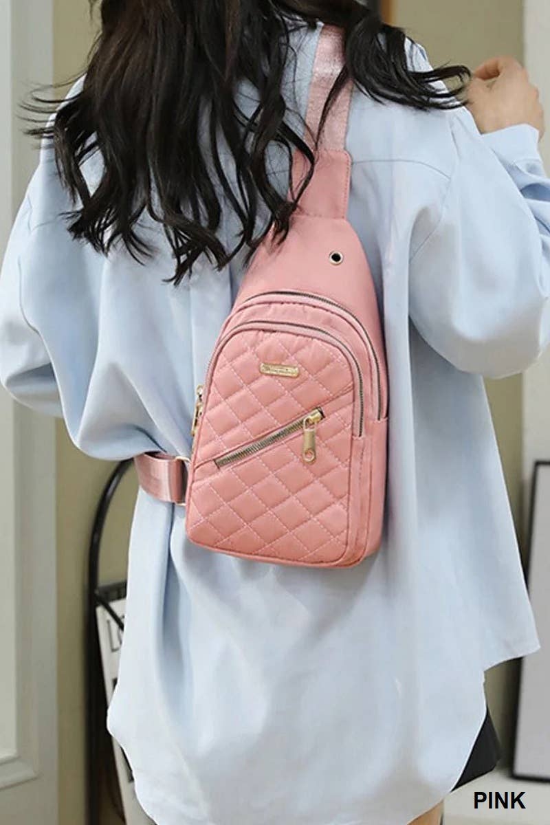 A woman wearing a light blue oversized shirt is shown with a quilted pink sling backpack. The compact bag features a sleek design with gold-tone zippers, a front zippered pocket, and an adjustable strap for crossbody or shoulder wear. Ideal for casual outings, the bag combines style and functionality in a soft pink color.