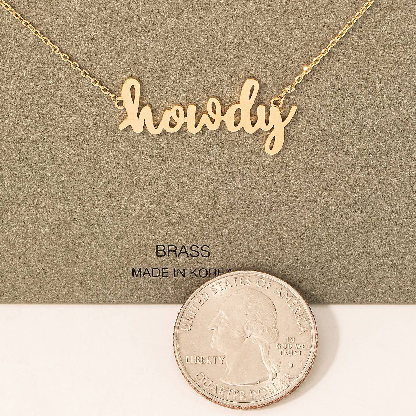 A minimalist gold-tone necklace featuring the word "howdy" in a playful, cursive font as the central pendant. The necklace is displayed on a simple olive-green card with the text "BRASS" and "Made in Korea" printed below. A stylish and charming accessory perfect for casual wear or gifting.