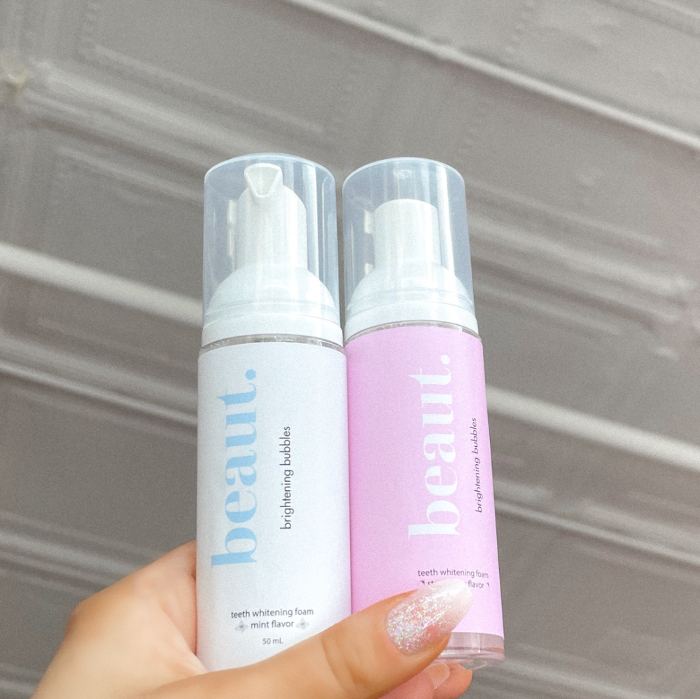 Beaut Brightening Bubbles teeth whitening foam in 50 mL bottles. Features a sleek design in pastel pink (strawberry flavor) and light blue (mint flavor), with matching minimalistic packaging. Promotes a fresh and radiant smile with a playful, modern aesthetic.
