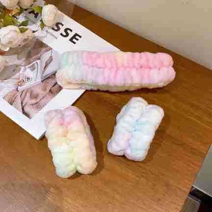 Soft and fluffy pastel rainbow spa headband and matching wristbands displayed on a wooden surface, perfect for keeping hair and hands dry during skincare routines.