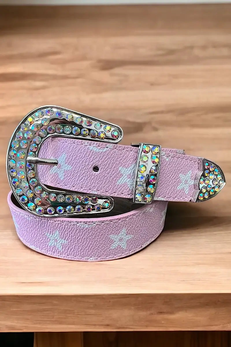 "Pink belt with a silver, rhinestone-encrusted buckle and white star patterns, displayed on a wooden surface."