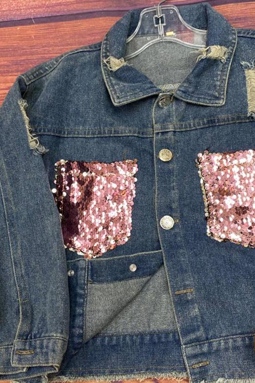 Trendy girls' denim jacket featuring pink sequin embellishments on the front pockets and distressed detailing for a stylish, modern look. Paired with brown suede fringe boots with gold stud accents, this outfit is perfect for casual outings, fall fashion, or statement kid’s clothing. Set against a rustic wood backdrop for a chic presentation.