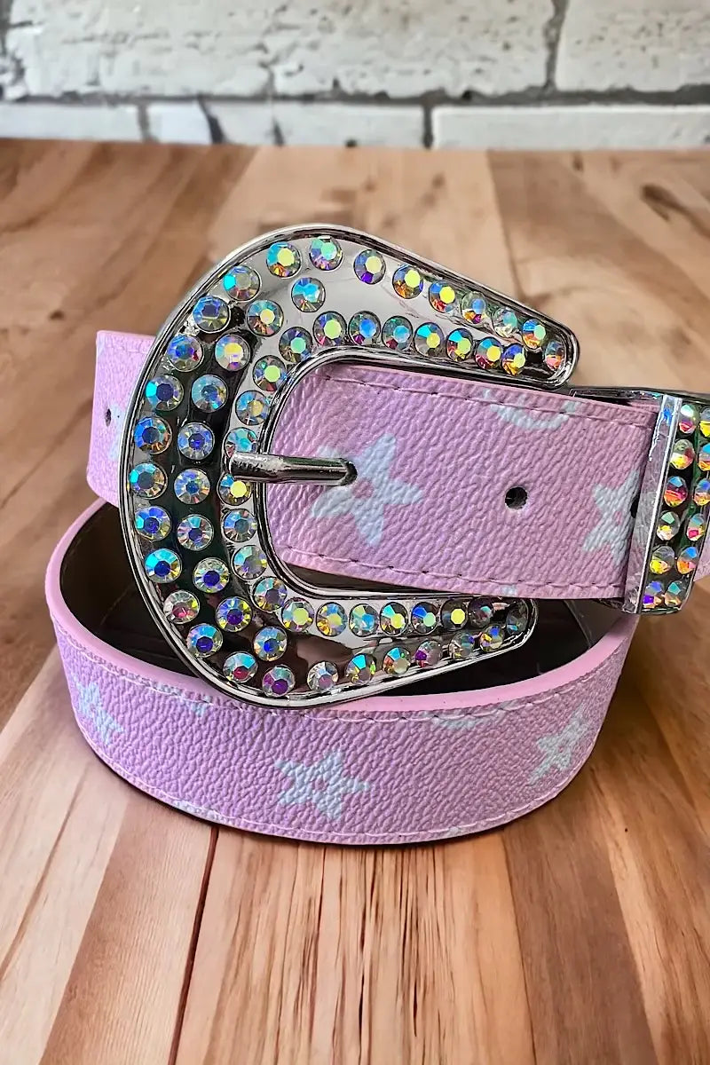 "Pink belt with a silver, rhinestone-encrusted buckle and white star patterns, displayed on a wooden surface."