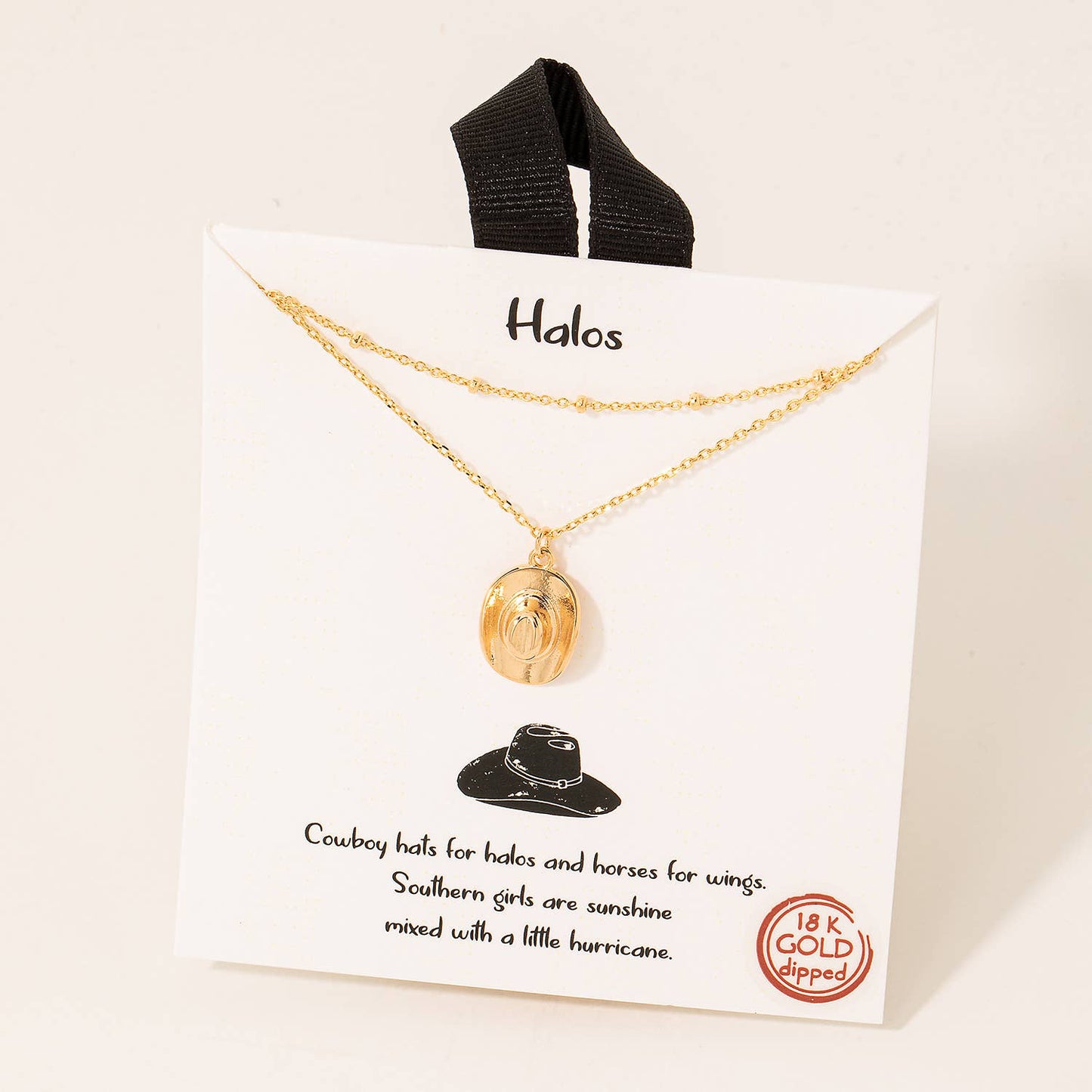 Gold layered necklace with a cowboy hat pendant on a branded display card featuring text "Cowboy hats for halos and horses for wings. Southern girls are sunshine mixed with a little hurricane," with an 18K gold-dipped label.