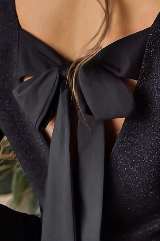 Elegant black shimmer top featuring a low back design adorned with a large satin bow detail. The long bow ties add a touch of sophistication, perfect for evening wear or special occasions. The glittery fabric enhances its chic appeal, complementing the fitted silhouette.