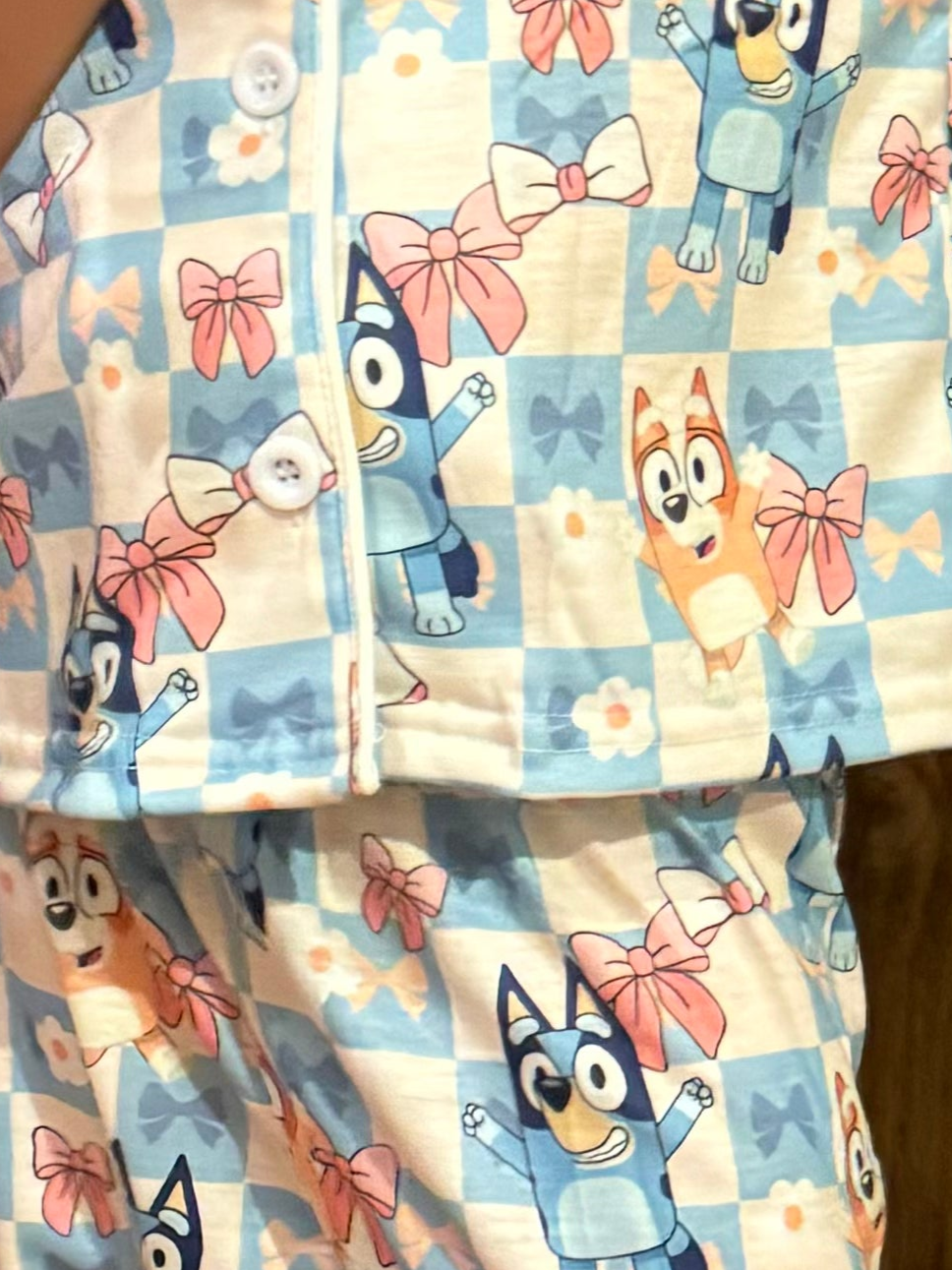 a close up of the pajama sets adorned with bluey and bingo, bows, and flowers in a pastel checkered pattern