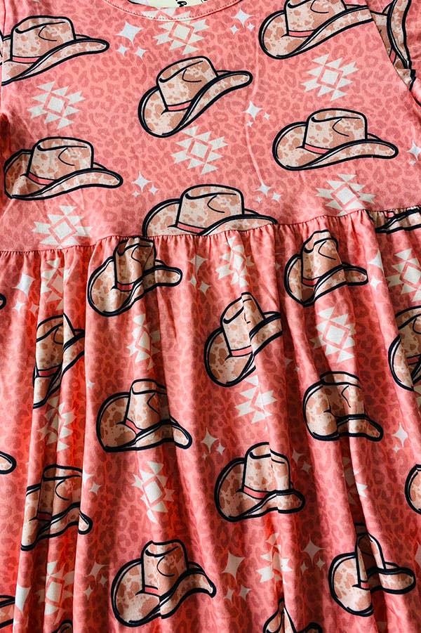 Pink short-sleeve dress with a Western-themed design featuring cowboy hats and geometric patterns, paired with a black fringe crossbody bag for a playful, country-inspired outfit. Displayed on a soft white textured background.