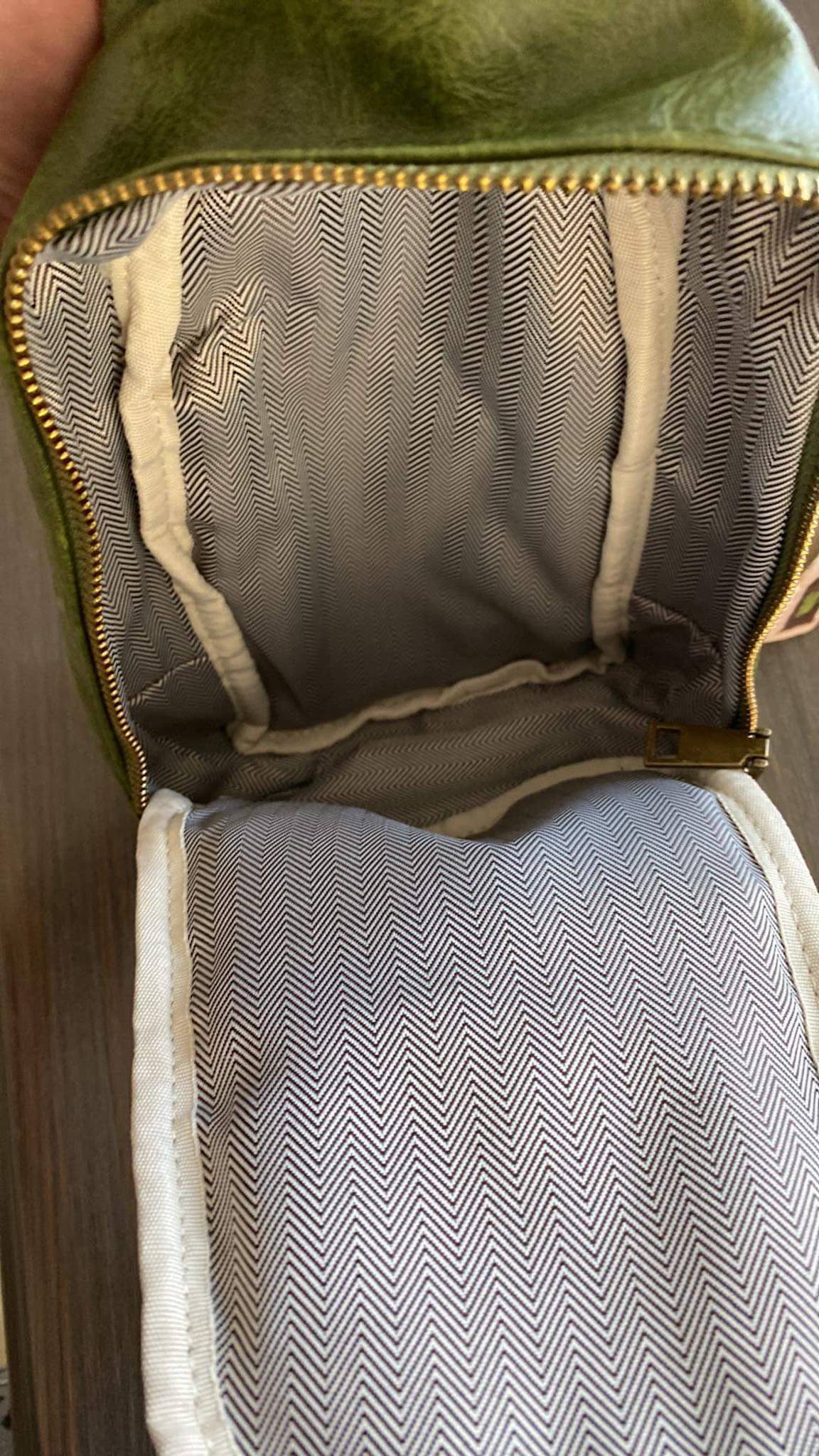 Alt text: A beige faux-leather sling bag with a zipper closure and a patterned strap featuring a tan and white zigzag diamond design. The bag is displayed on a dark wooden surface, showcasing its minimalist and stylish design.