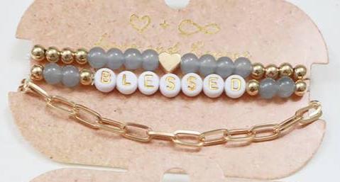 Set of elegant bracelets featuring gold beads, gray beads, and a white letter bead design spelling 'BLESSED.' The set includes a dainty gold heart accent and a stylish gold chain bracelet, displayed on a rustic beige backing card with a minimalist heart design, perfect for gifting or accessorizing with a positive touch.