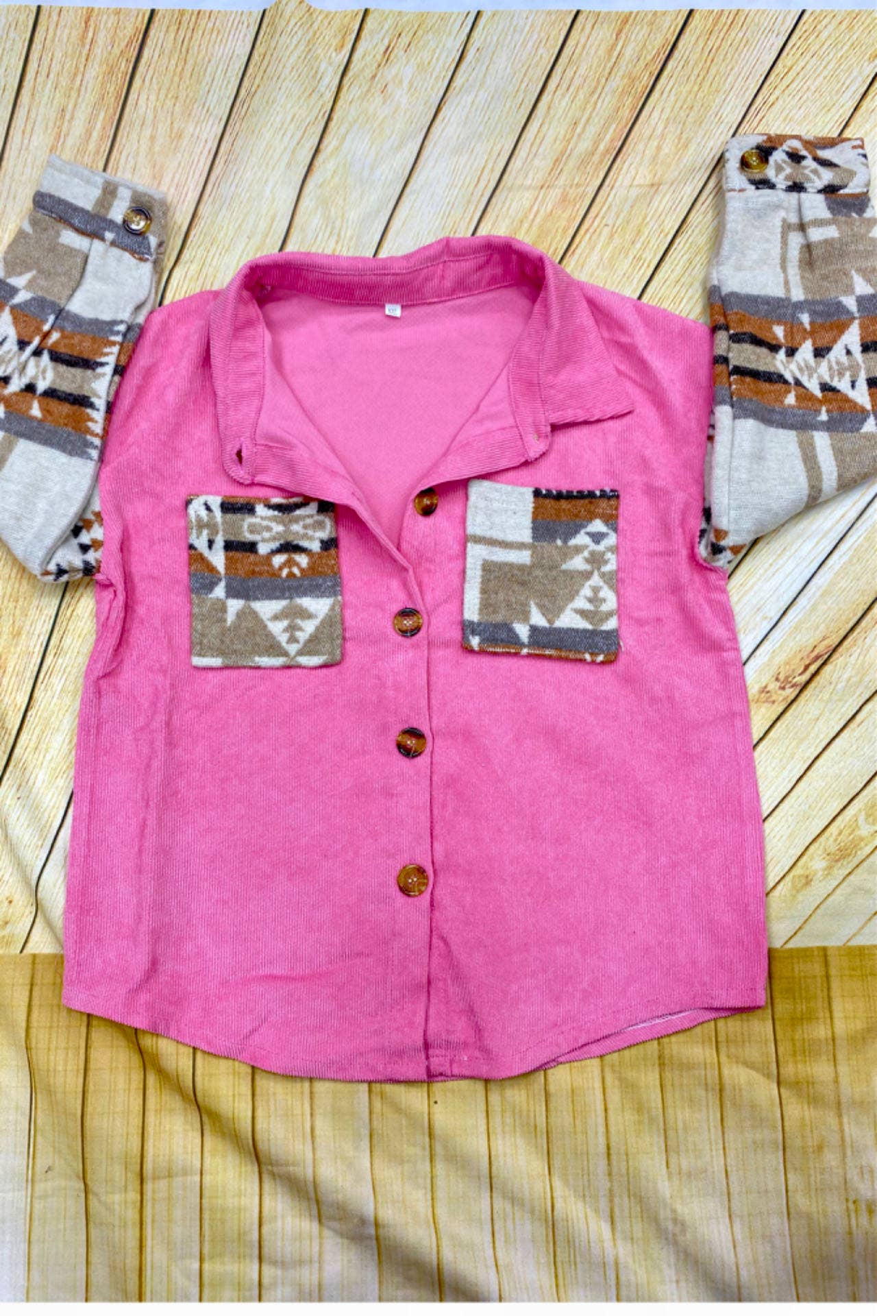 "Child wearing a pink corduroy shacket with patterned sleeves and pockets, paired with a white knotted top, blue jeans, and brown cowboy boots, standing in front of a wooden barn door."