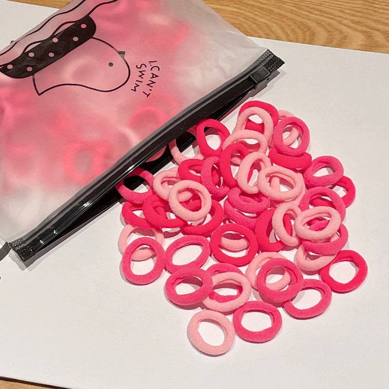 A small plastic zippered bag labeled "I Can Swim" is open, spilling out a colorful assortment of hair ties onto a white surface. The hair ties come in different shades of pinks, creating a vibrant and playful display.