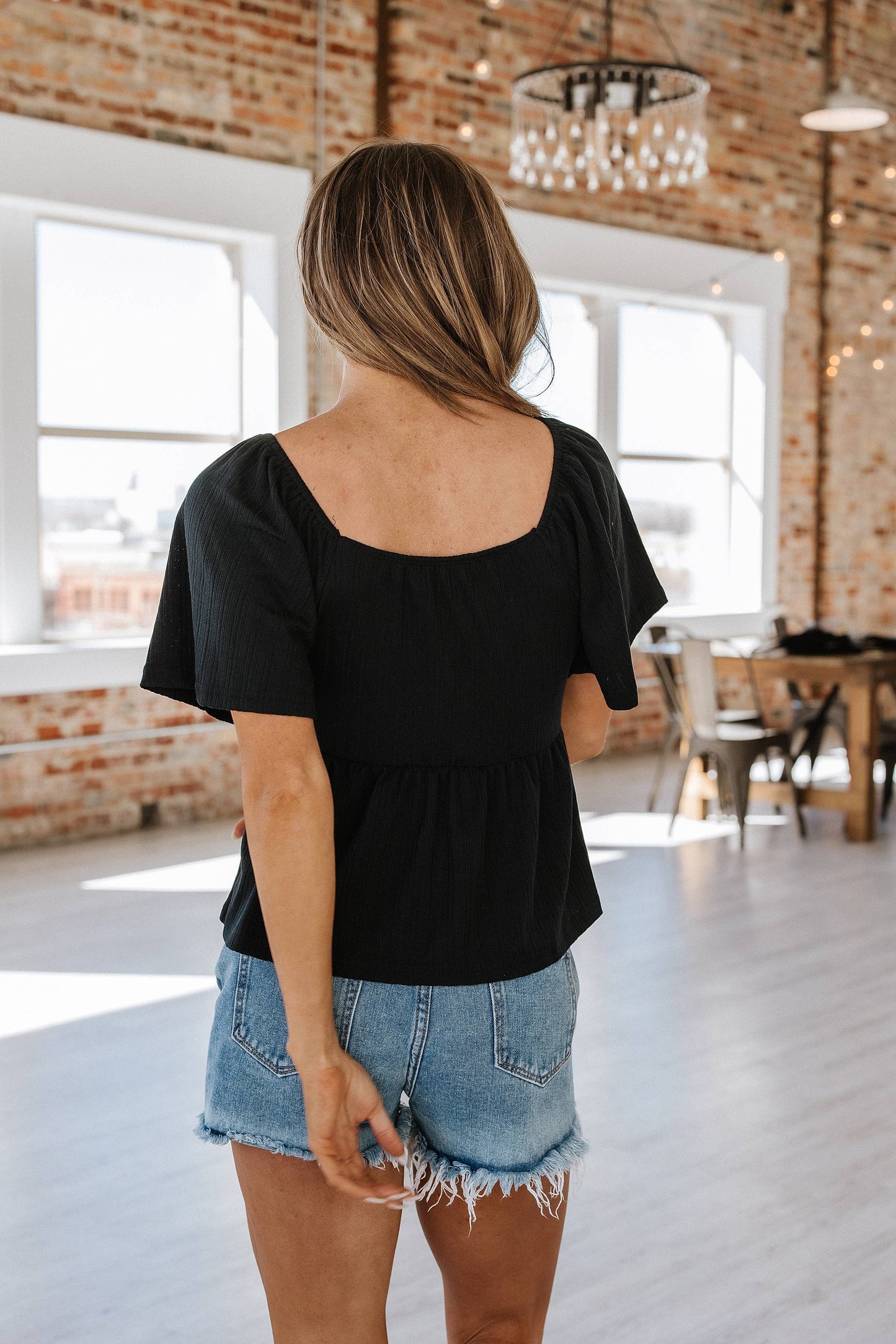 Image of a charming babydoll blouse featuring delicate flutter sleeves. This blouse has a loose, flowing silhouette with a high empire waistline that gently flares out, creating a flattering and comfortable fit. The flutter sleeves add a soft, feminine touch, while the babydoll style gives it a relaxed, airy feel. Made from a lightweight fabric, this blouse is perfect for pairing with jeans, skirts, or shorts for a casual yet polished look.