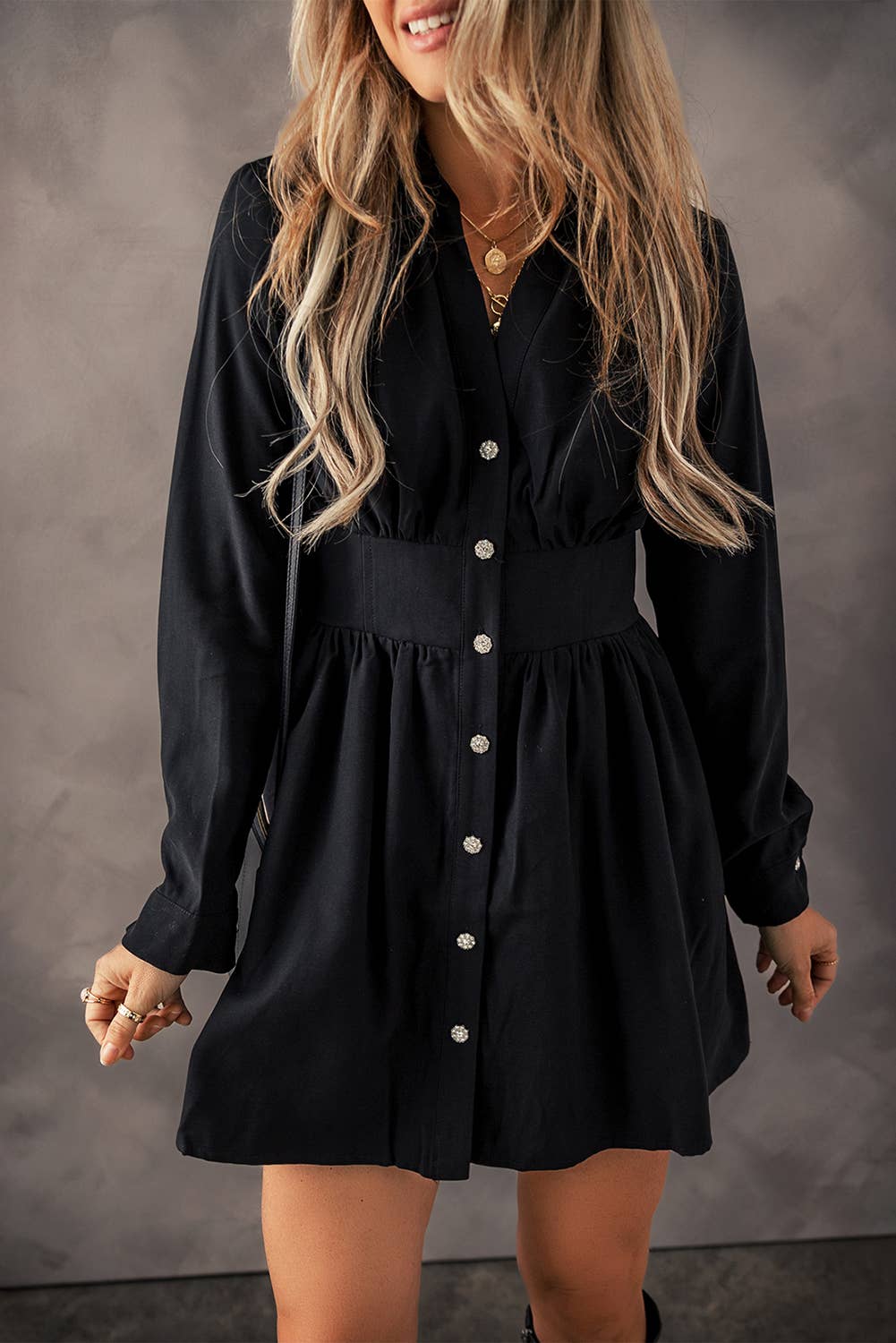 Stylish black button-down mini dress with a cinched waist and long sleeves, featuring delicate floral buttons. Perfect for a chic and versatile look, ideal for casual outings or dressed-up occasions. This little black dress combines comfort and elegance, making it a must-have staple for women's fall fashion