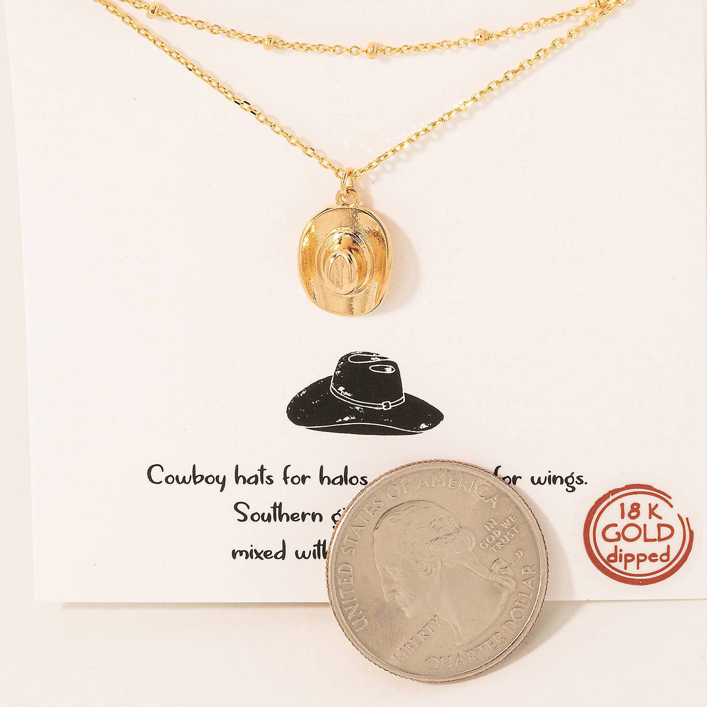 Gold layered necklace with a cowboy hat pendant on a display card, including text and a US quarter for size reference. The card reads, "Cowboy hats for halos and horses for wings. Southern girls are sunshine mixed with a little hurricane," with an 18K gold-dipped label.