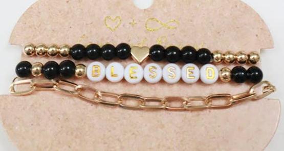 Set of elegant bracelets featuring gold beads, black beads, and a white letter bead design spelling 'BLESSED.' The set includes a dainty gold heart accent and a stylish gold chain bracelet, displayed on a rustic beige backing card with a minimalist heart design, perfect for gifting or accessorizing with a positive touch.