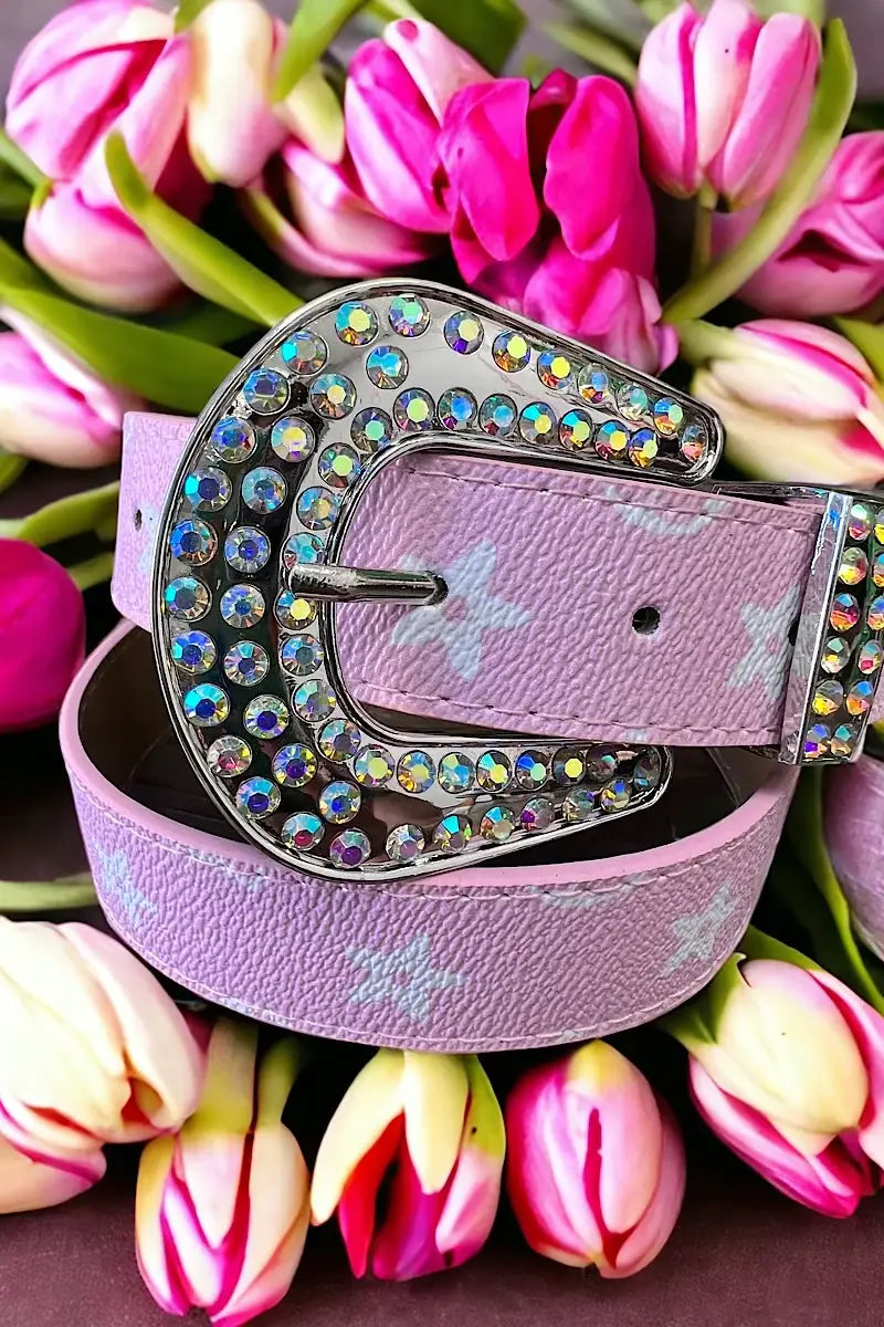 "Pink belt with a silver, rhinestone-encrusted buckle and white star patterns, displayed on a wooden surface."