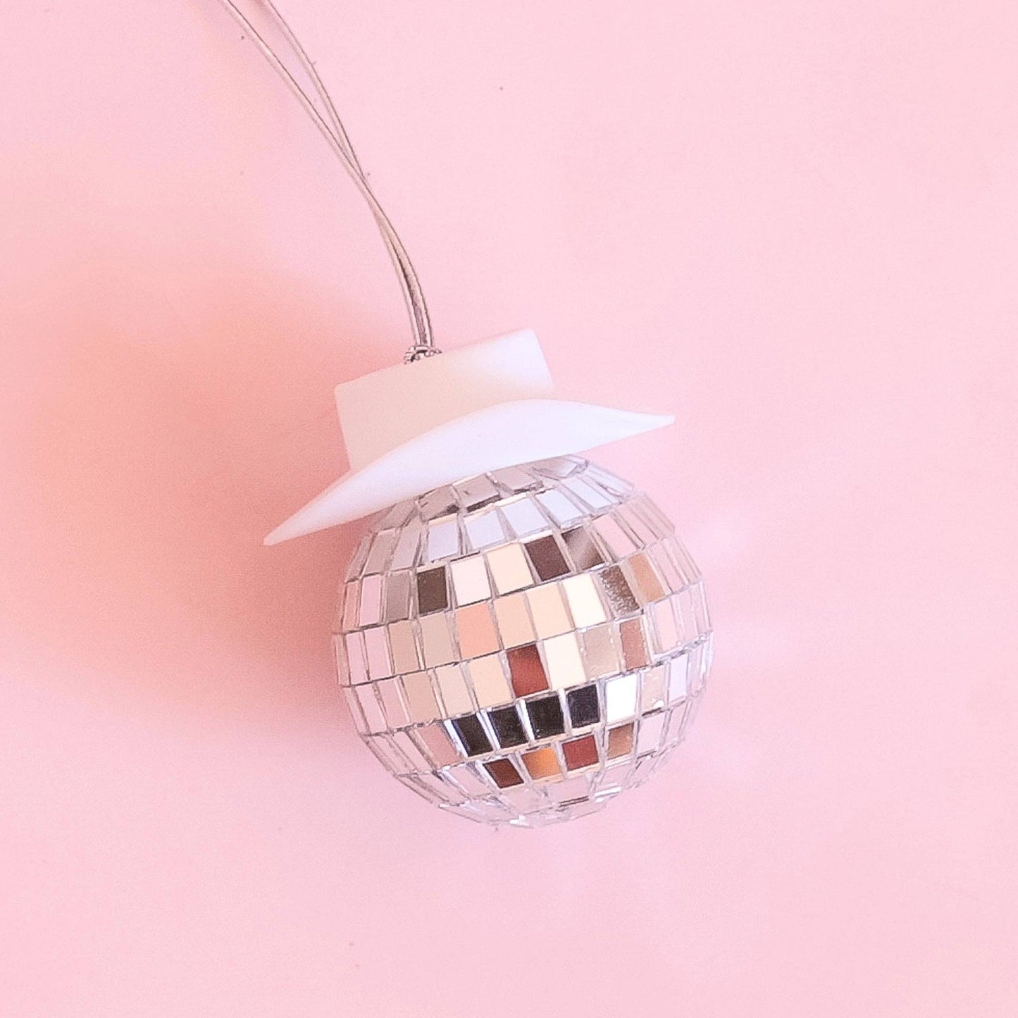A stylish disco ball ornament featuring reflective mirrored tiles and topped with a white cowboy hat, hanging on a silver string. Perfect for adding a fun, festive, and Western-inspired touch to holiday decor or party themes.