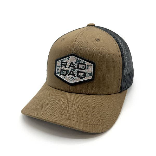 A brown version of the same trucker-style cap, also featuring the "RAD DAD" hexagonal camouflage patch. The structured front pairs with a black mesh back and a curved brim, maintaining the cap's rugged and versatile aesthetic.