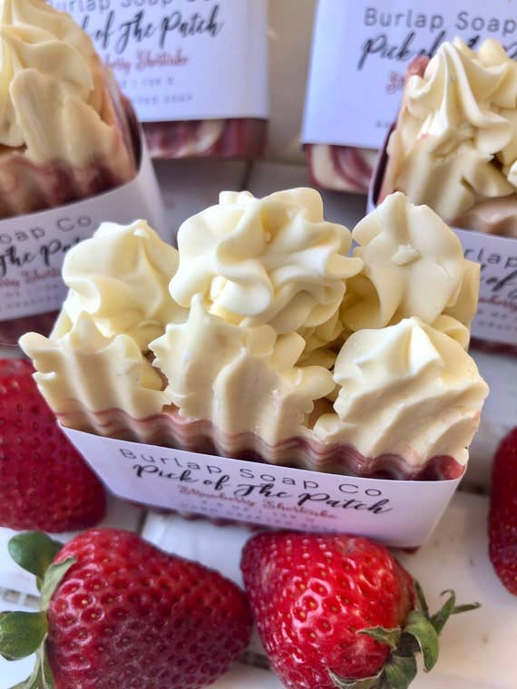 A detailed view of the "Strawberry Shortcake" soap bars showcasing the intricate swirled design of creamy white and berry pink tones, mimicking layers of dessert. The soap is styled alongside plump, ripe strawberries, emphasizing the sweet and fruity theme.