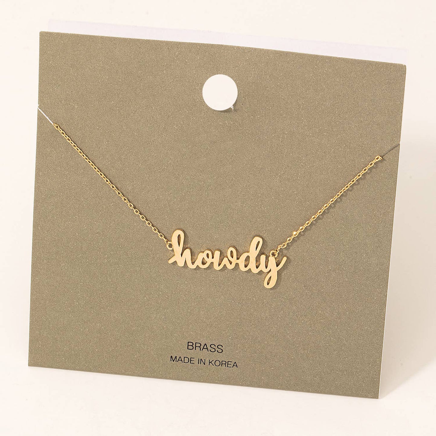 A minimalist gold-tone necklace featuring the word "howdy" in a playful, cursive font as the central pendant. The necklace is displayed on a simple olive-green card with the text "BRASS" and "Made in Korea" printed below. A stylish and charming accessory perfect for casual wear or gifting.