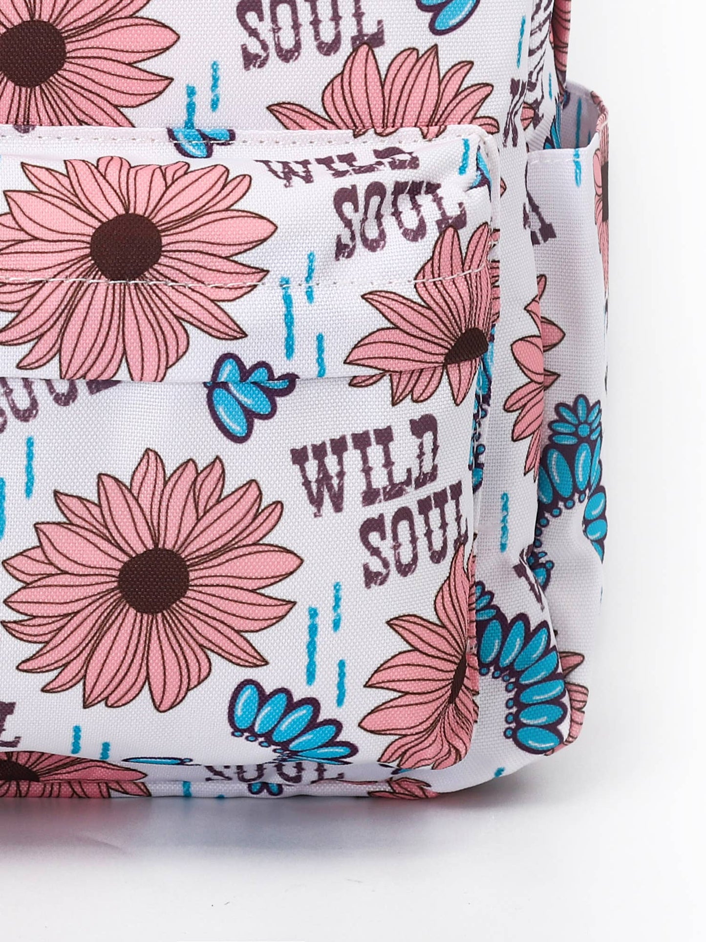 A detailed close-up image of a backpack showcasing its floral design featuring pink daisies with brown centers, blue accents, and the phrase "Wild Soul" printed throughout. The focus is on the stitching and front pocket.
