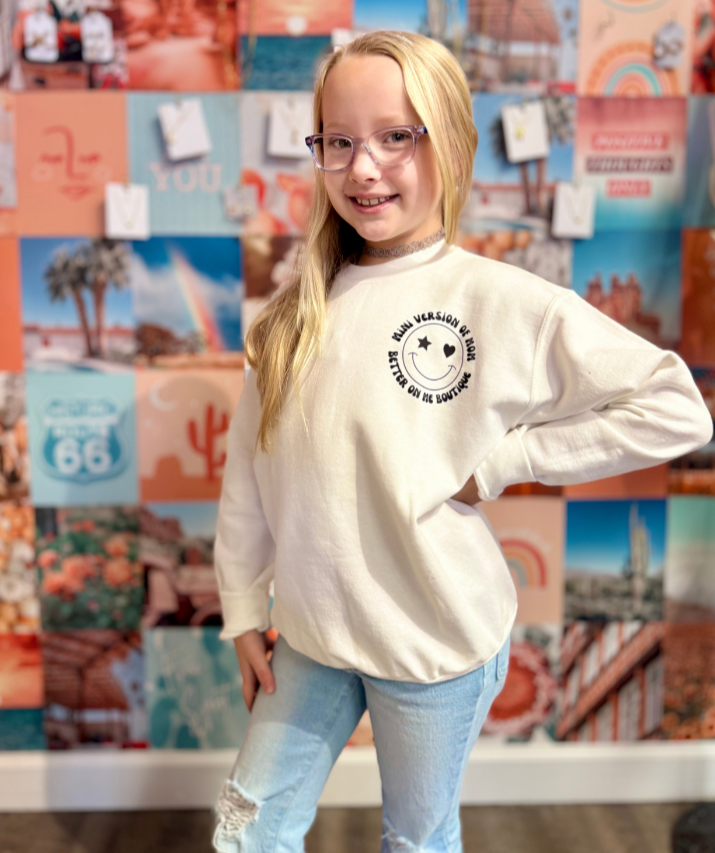 Young girl wearing a white sweatshirt with 'Miniature Version of My Mom' text and floral accents, styled with light-wash jeans.