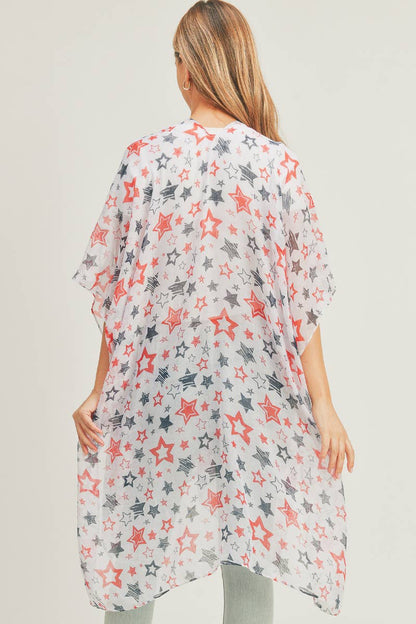 A woman modeling a lightweight, sheer kimono with a patriotic star pattern in red, navy blue, and white. The open-front kimono features a flowing, loose-fit design that drapes effortlessly over a white ribbed top and light-wash jeans. Perfect for layering during casual outings or holiday events, offering a stylish yet breezy look.