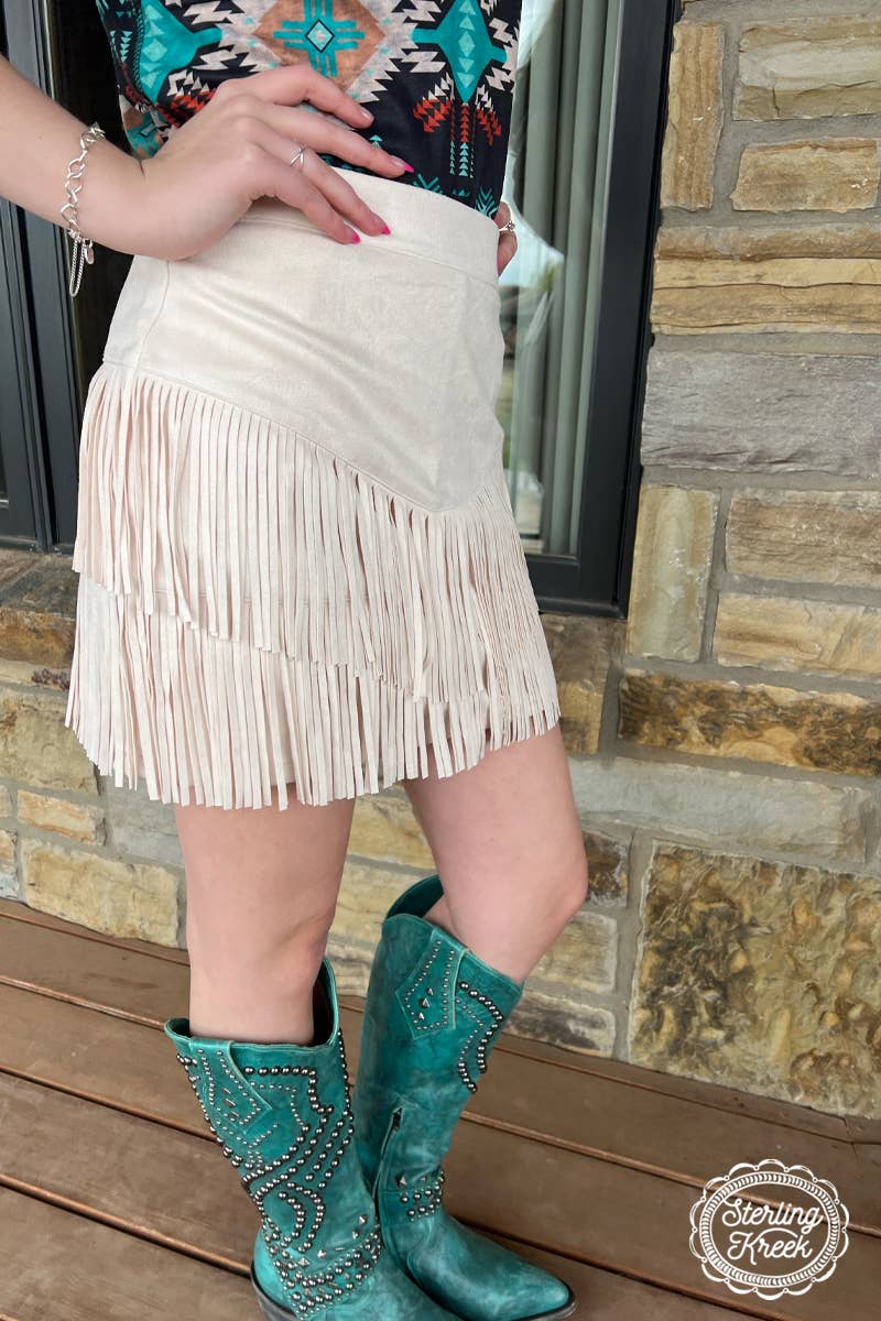 
Image of a cream-colored western fringe skirt, featuring a soft, neutral tone that adds a touch of boho-chic to any outfit. The skirt is designed with playful fringe detailing that flows along the hem, creating movement and a relaxed, carefree vibe. The lightweight fabric and flattering fit make it perfect for pairing with boots, sandals, or a tucked-in graphic tee for a laid-back, stylish look.